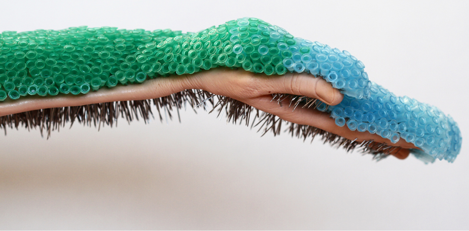 Hand extended horizontally across a plain background, holding hundreds of green and blue needles