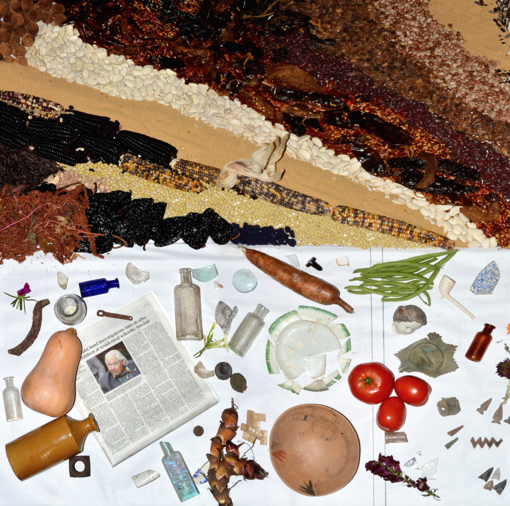 Collage of corn stalks and various found items scattered over a white cloth