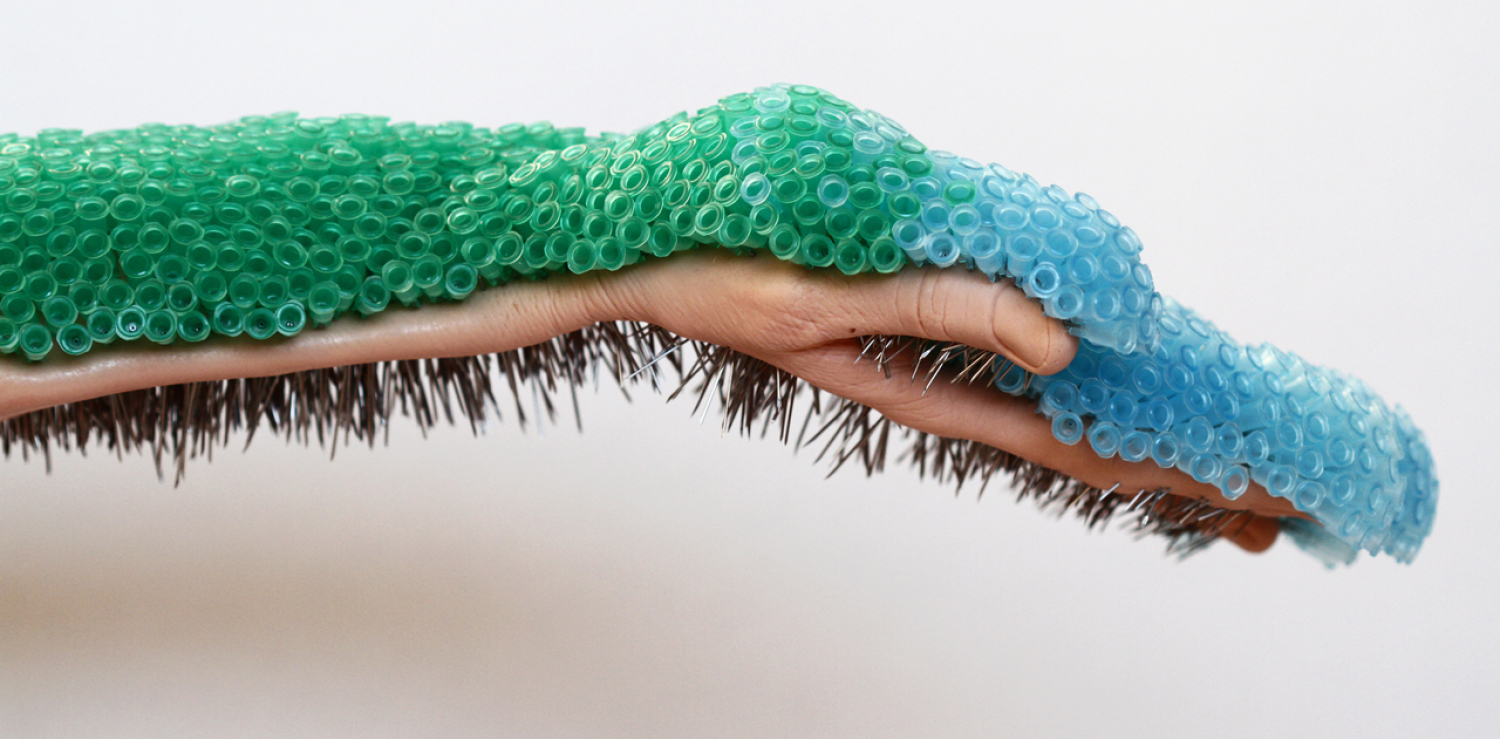 Hand extended horizontally across a plain background, holding hundreds of green and blue needles