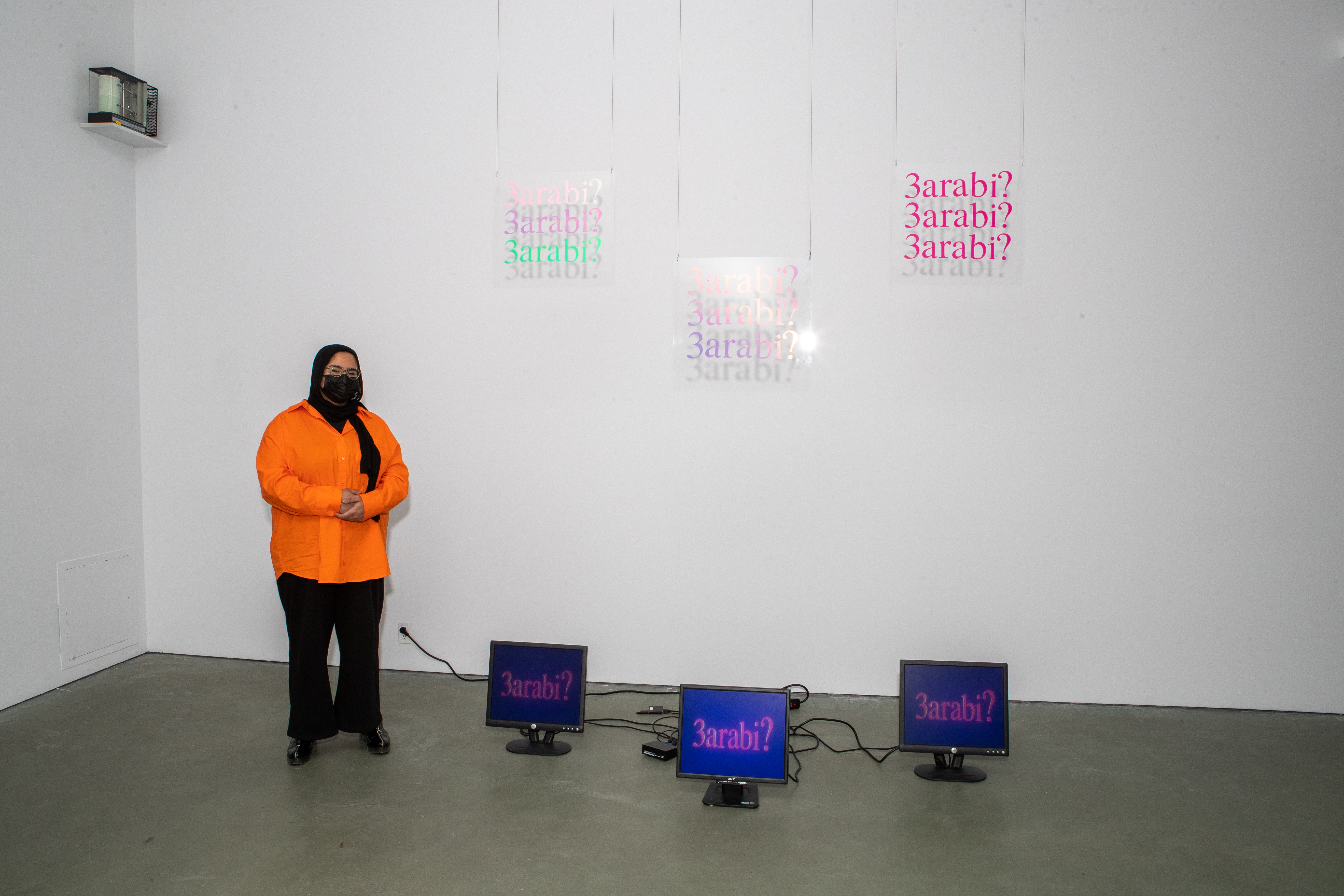 A student in front of three plex glass pieces of art handing from the wall and three tv monitors on the floor
