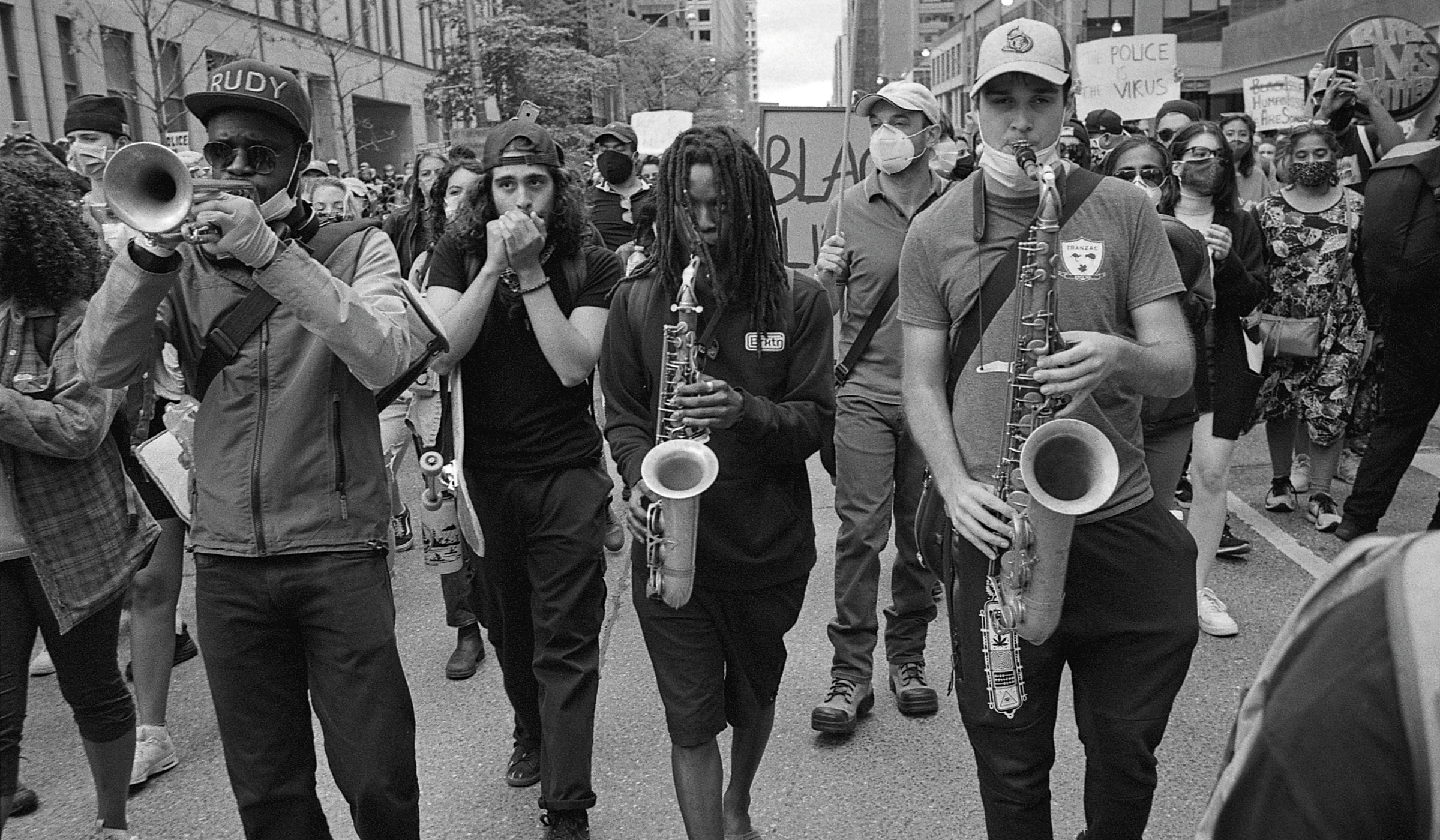 Black and white photograph of a crowd marching down a street playing instruments