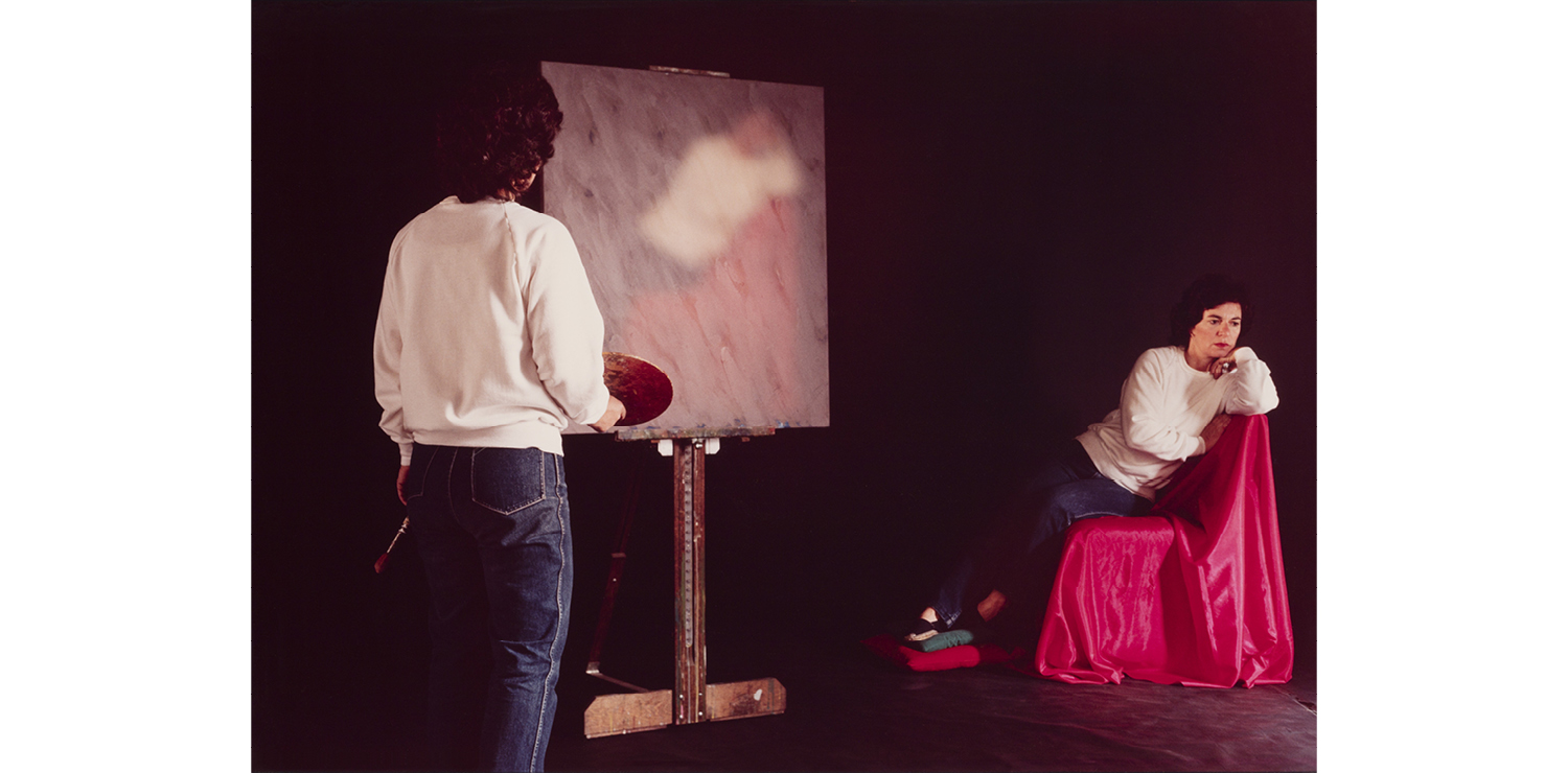 A person in a white sweater and jeans stands in front of a canvas with a paint palette. Beside them on the right is their subject in the same outfit posed on a red draped chair.