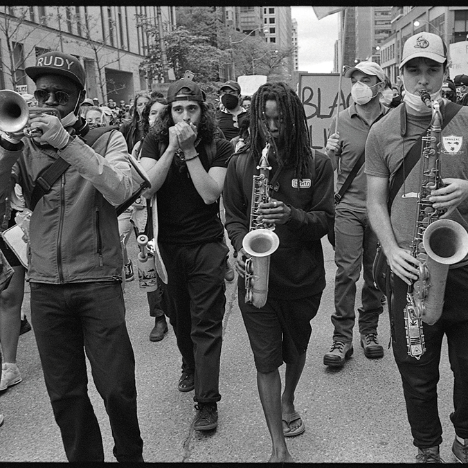 Black and white photograph of a crowd marching down a street playing instruments