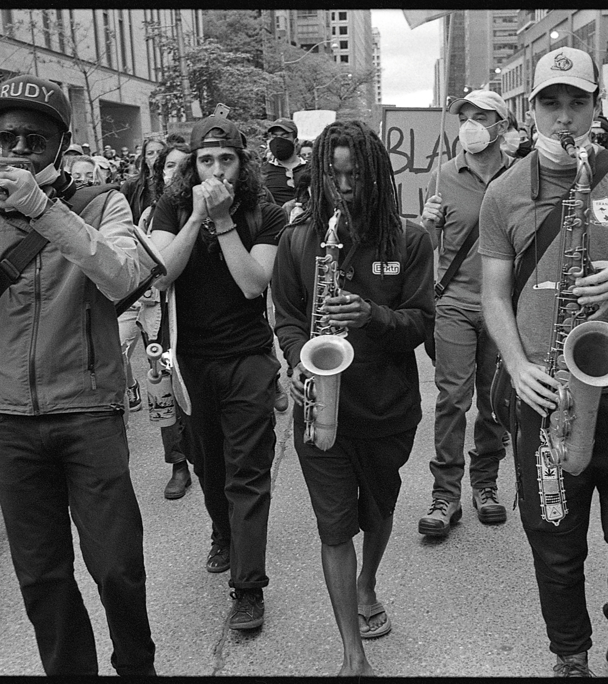 Black and white photograph of a crowd marching down a street playing instruments