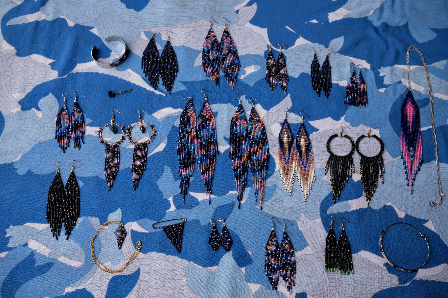 A series of beaded earrings laid out on a tablecloth of abstract cool blue tones and pattersn