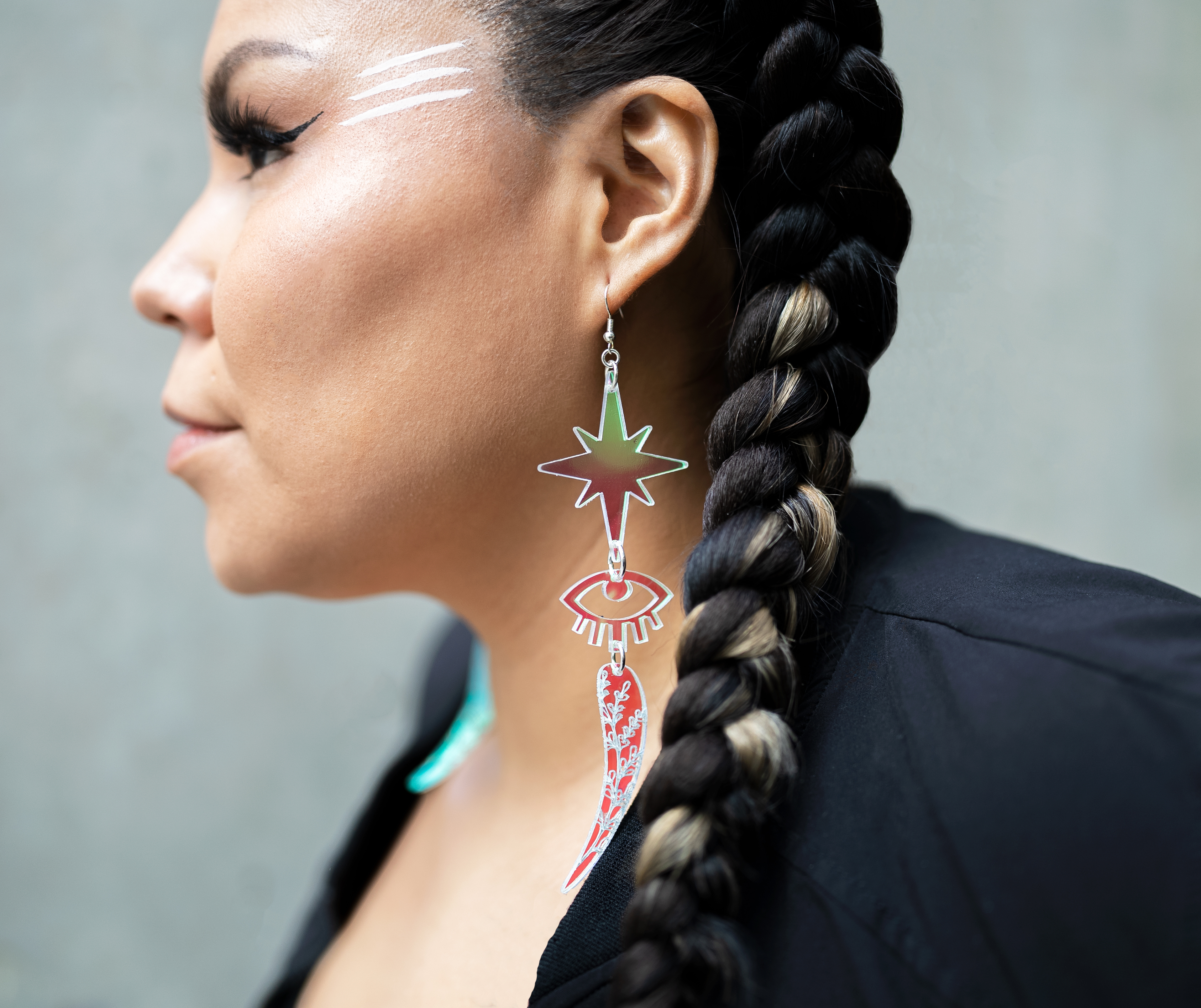 Image of person with long dark braids wearing a pair of long artisan crafted earrings