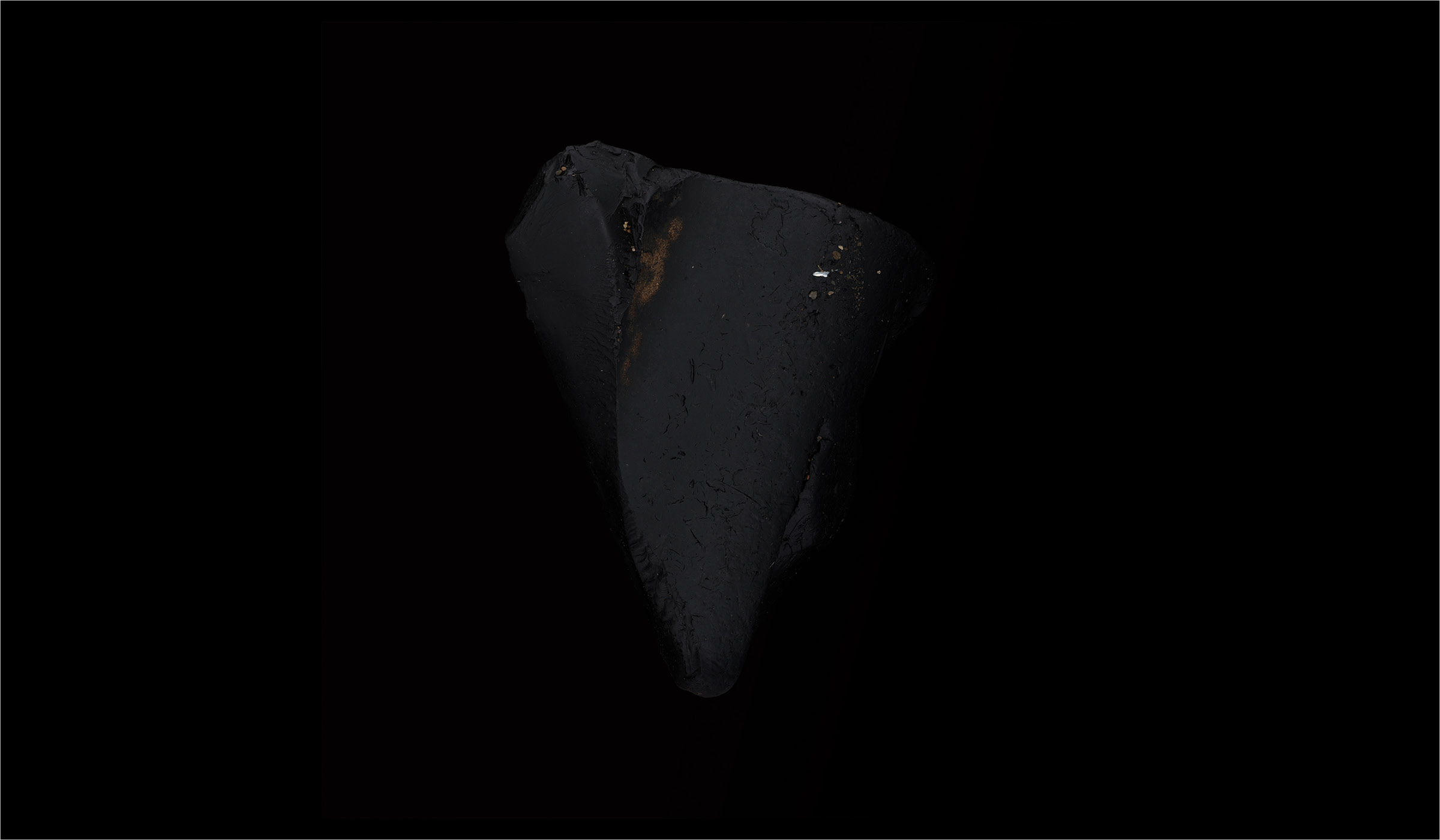 A black, cone shaped piece of earthen material floating against a black background