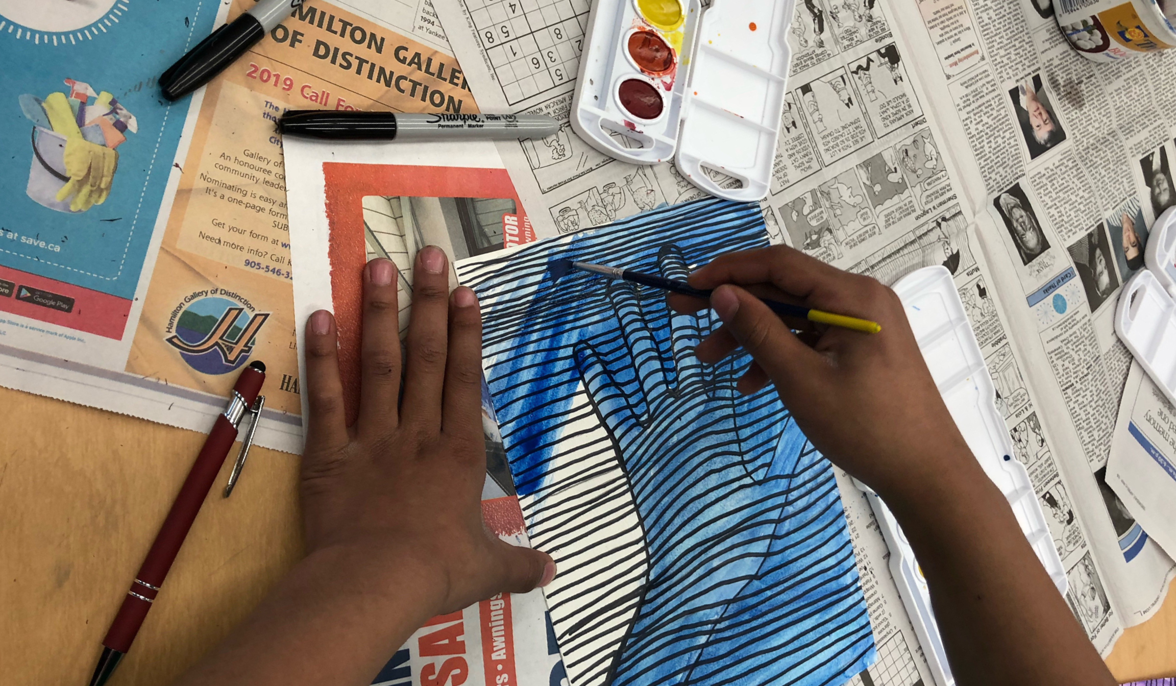 Student hands painting a striped artwork of a hand.