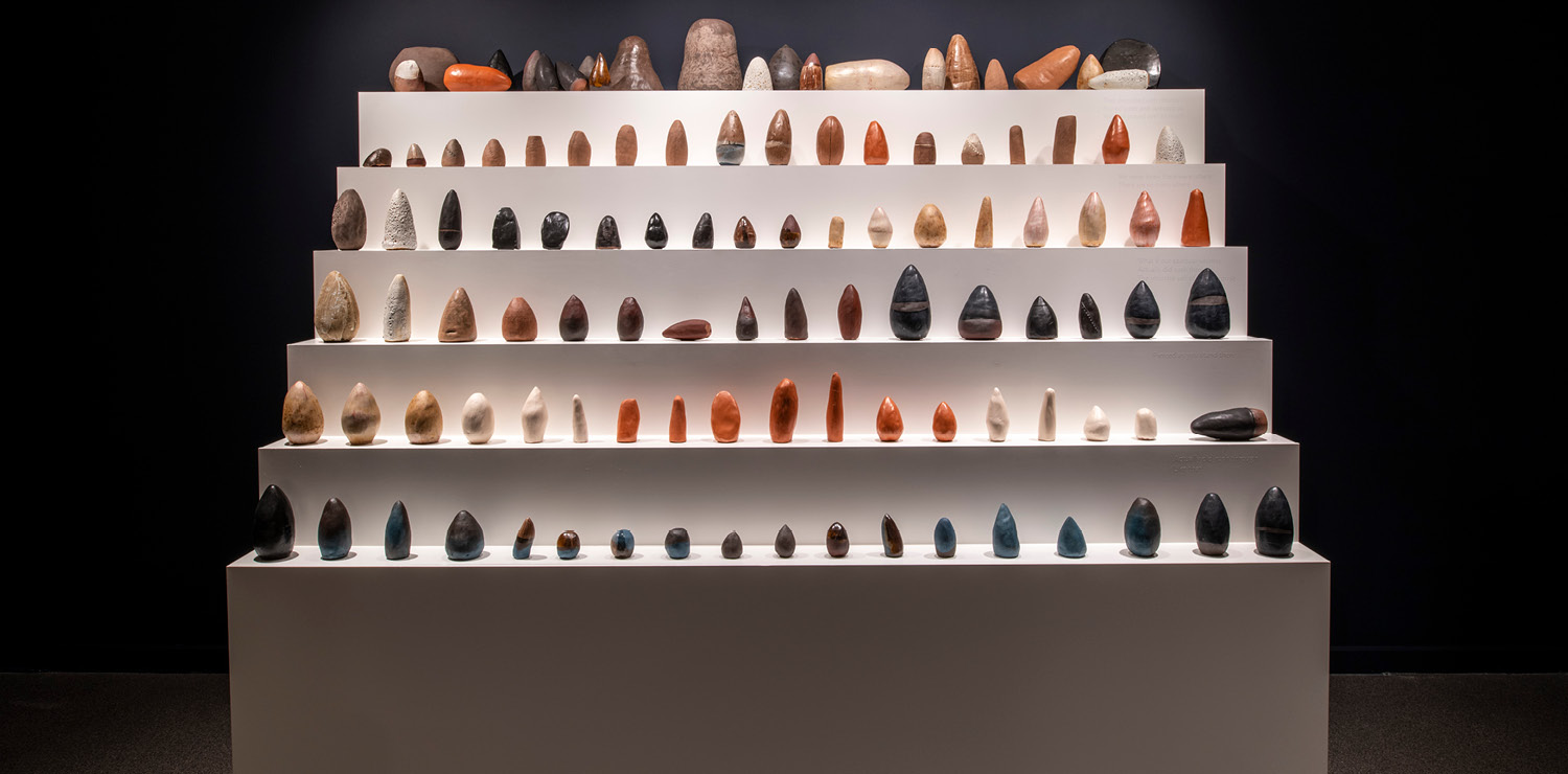 A series of small ceramics and pottery arranged neatly in rows on a 6-stepped white platform.