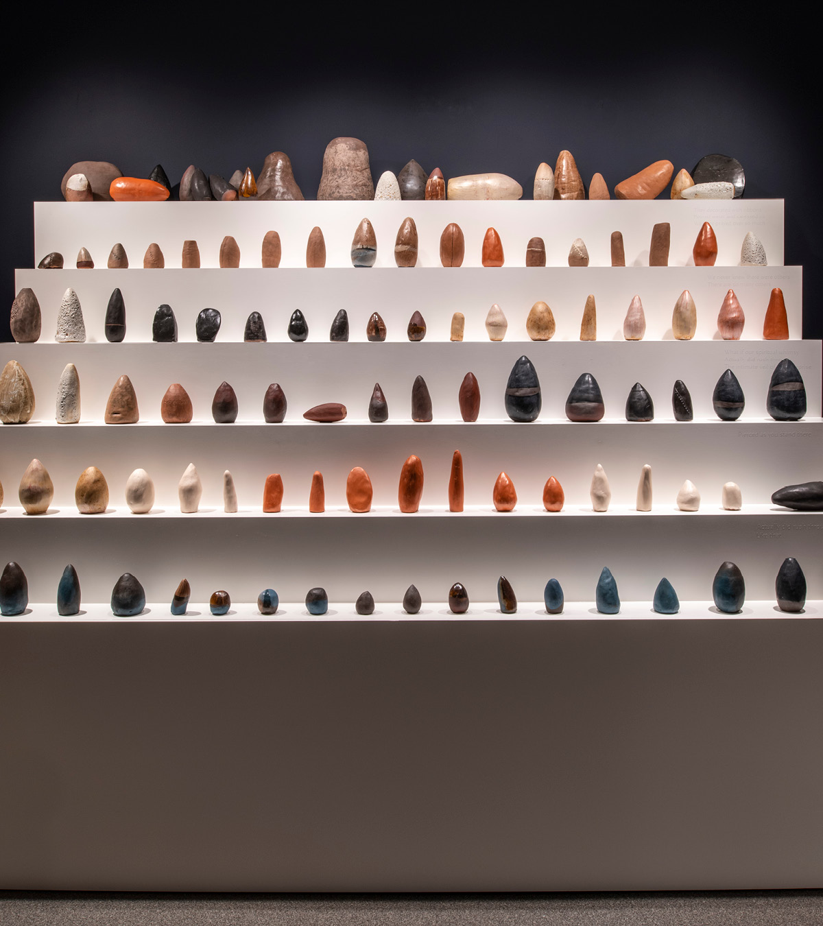 A series of small ceramics and pottery arranged neatly in rows on a 6-stepped white platform.